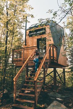 a woman standing on top of a wooden staircase next to a tree house in the woods