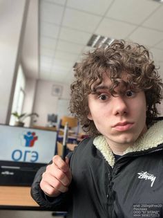 a young man with curly hair is posing for the camera in front of a computer screen