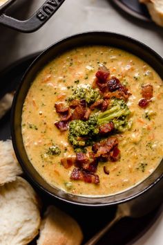 a bowl of soup with bacon and broccoli in it next to some bread