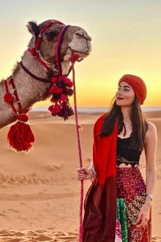 a woman standing next to a camel in the desert