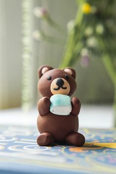 a small brown bear holding a cupcake in it's mouth sitting on a table