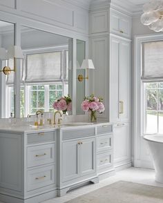 a white bathroom with two sinks and a bathtub in the middle, along with large windows