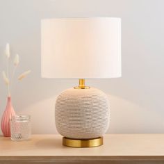 a white lamp sitting on top of a wooden table next to a vase with flowers