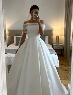 a woman in a white wedding dress taking a selfie with her cell phone while standing in front of a bed