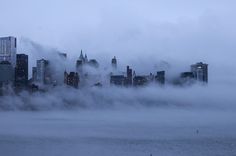 fog covers the city skyline as it sits in the middle of the water on a cloudy day