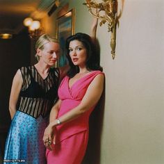 two women standing next to each other in front of a wall with a chandelier