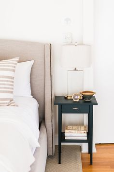 a nightstand with two books on it next to a bed