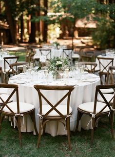 a table set up with white linens and wooden chairs for an outdoor wedding reception