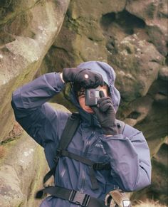 a man taking a photo with his cell phone in front of some rocks and grass