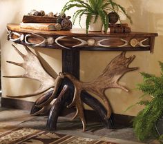 a wooden table with antlers and plants on it's side stand in front of a wall