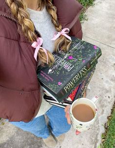 a woman holding a cup of coffee and some books