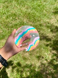 a hand holding a donut with rainbow frosting and stars on it in the grass