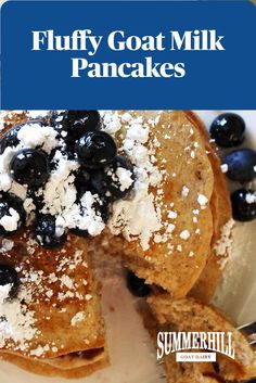 fluffy goat milk pancakes topped with blueberries and powdered sugar on a white plate