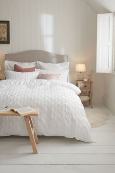 a bed with white comforter and pillows in a room next to a table on the floor