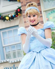 a woman dressed in a blue dress and white gloves is smiling while holding her hands together