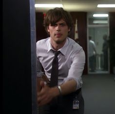 a young man in a tie leaning against a wall with his hand on the door