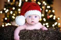 a baby wearing a santa hat sitting in front of a christmas tree