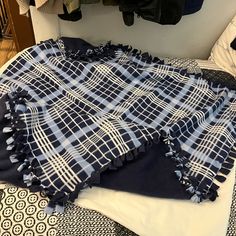 an unmade bed with blue and white plaid blankets on it, next to clothes hanging in the closet