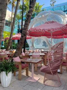 an outdoor dining area with pink chairs and umbrellas in front of a large white ball