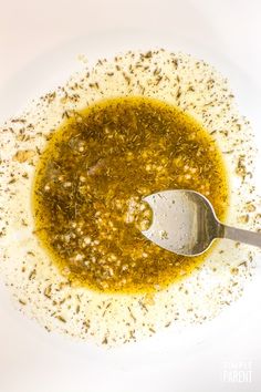 a white bowl filled with olive oil and seasoning next to a spoon on top of it