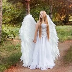 a woman with long hair wearing an angel costume standing on a path in the woods