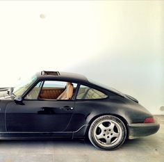 a black porsche sports car parked in a white walled room with no one around it