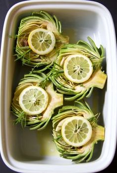 some lemons and other vegetables in a white dish on a black counter top with water