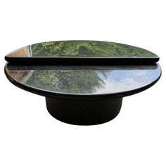 an oval glass table top with trees in the back ground and sky reflected on it