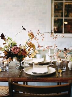 a table set with plates, glasses and vases filled with flowers on top of it