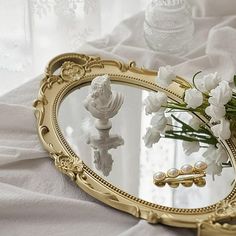 there is a mirror with flowers in it on the bed next to a glass vase