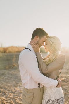 a man and woman standing next to each other on top of a dirt field with the sun behind them