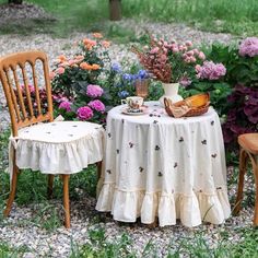 two wooden chairs sitting next to a table covered with a white tablecloth and flowers