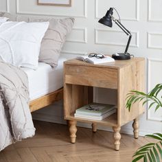 a bed with a wooden night stand next to it and a plant on the side