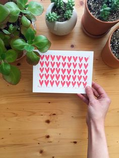 a person holding up a card with hearts on it next to some potted plants