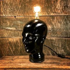 a black mannequin head with a light bulb on it's head sitting on a wooden table