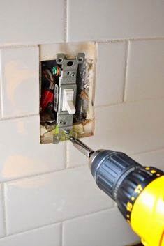 a person using a drill to fix an electrical outlet in a wall with white tiles