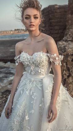 a woman in a wedding dress standing on the beach with her hair blowing in the wind