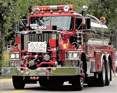 a red fire truck driving down a street with trees in the backgrouund