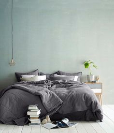 a bed with grey linens and white pillows in a green room next to a plant