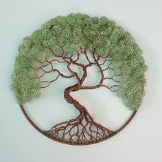 a wire tree sculpture is displayed on a white surface with green leaves and roots in the shape of a circle