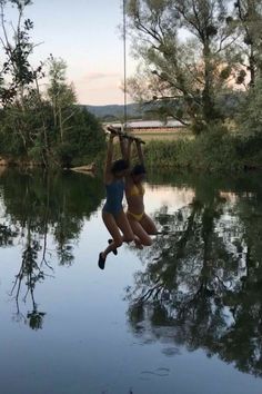 two girls are jumping into the water from a rope swing in front of trees and ducks