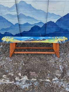 a wooden bench sitting in front of a wall with mountains and blue sky painted on it