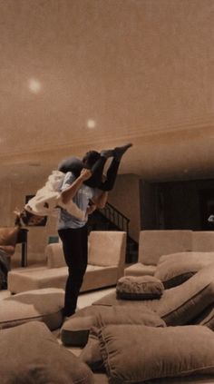 two people doing tricks on their skateboards in a living room filled with couches