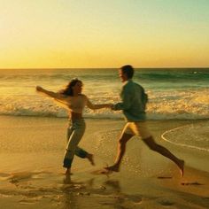 two people running on the beach at sunset with waves coming in and one person holding his hand