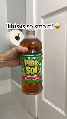 a hand holding a bottle of pine - soi in front of a toilet paper dispenser