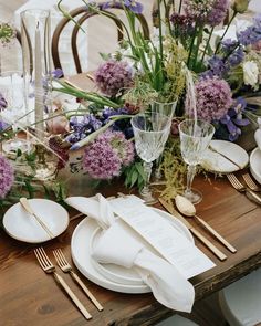 the table is set with white plates and silverware, purple flowers, and greenery