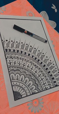 a pen sitting on top of a piece of paper next to a drawing pad with an intricate design