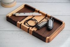 a wooden tray with two keys and a lighter on it, next to a cup