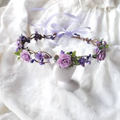 a white vase sitting on top of a bed covered in purple flowers and leaves next to a ribbon