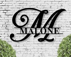 a sign that says m is for malone on a brick wall with two bushes in the foreground